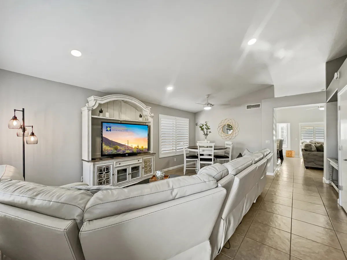A spacious living room featuring a comfortable sectional sofa positioned in front of a large TV, with a decorative cabinet nearby and a dining area visible in the background. The room exudes a relaxed, welcoming atmosphere ideal for group gatherings or movie nights.