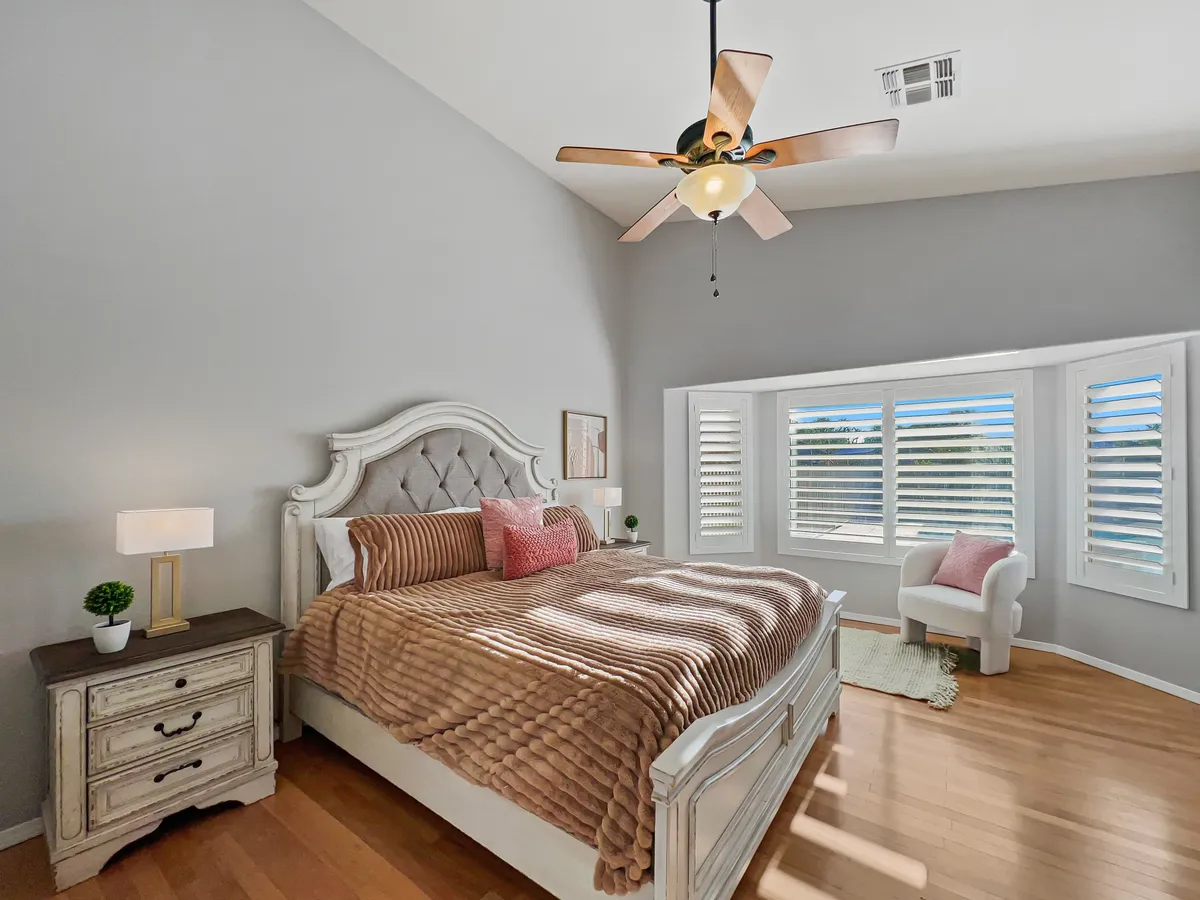 A tranquil bedroom scene featuring a plush bed with soft bedding, a bay window seating area flooded with natural light, and a decorative lamp on the nightstand. The atmosphere is cozy, serene, and inviting—ideal for relaxing after a long day.