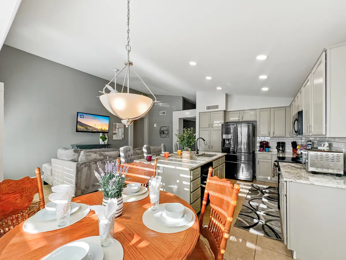 This image features a dining table set for a meal, a kitchen island with modern appliances, and a comfortable living area in the background. The scene captures the heart of the home, where cooking, dining, and gathering seamlessly blend together.