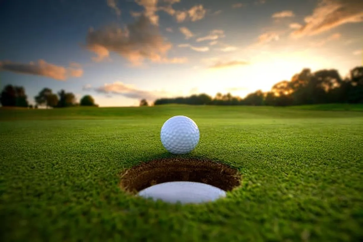 A close-up view of a golf ball poised at the edge of a golf hole, set on lush, vibrant green grass. The scene is serene and reflective, capturing the essence of a day spent golfing outdoors.