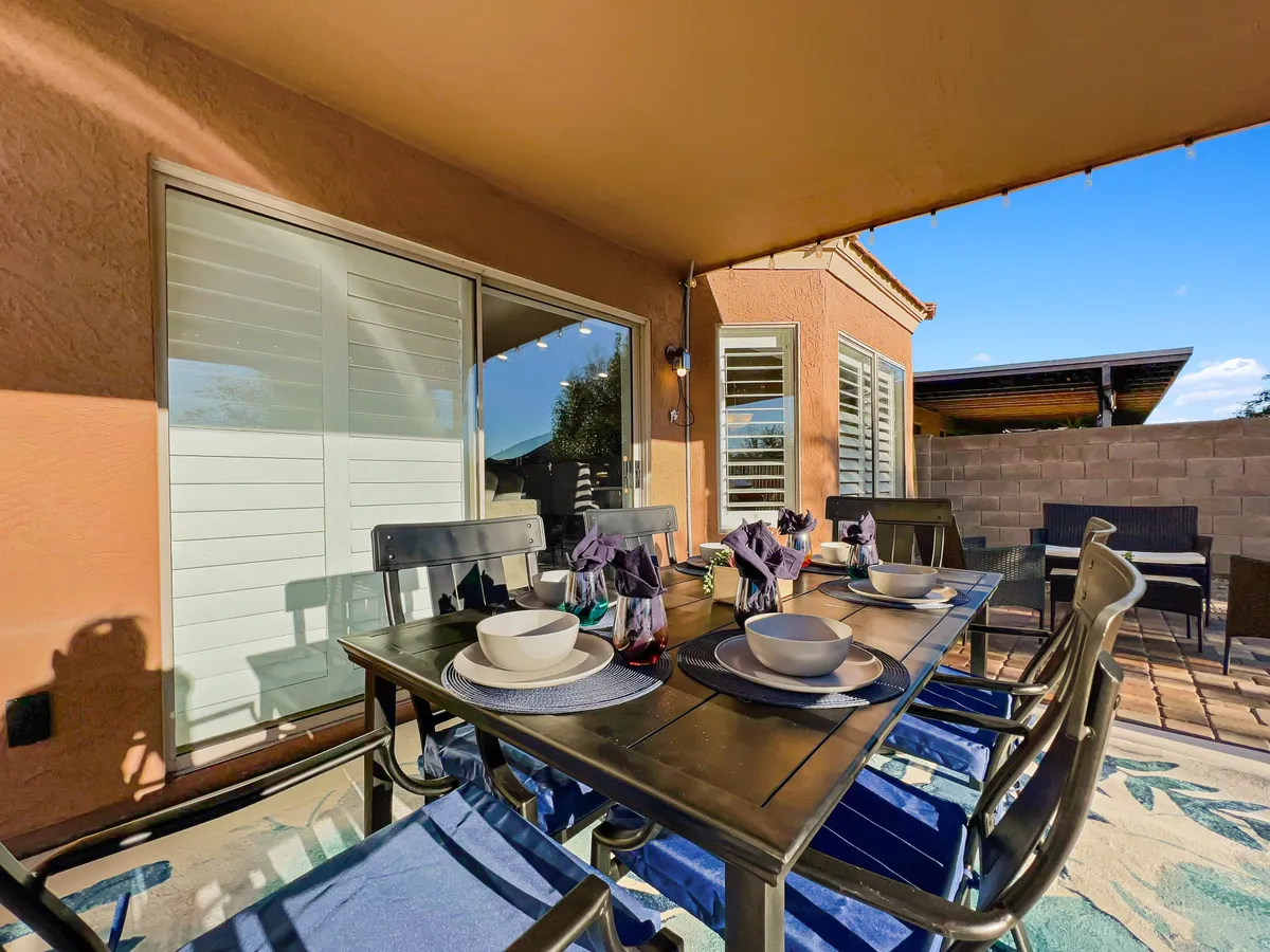 A beautifully set outdoor dining table under a covered patio, complete with decorative accents and comfortable seating. The scene is bright and lively, perfect for entertaining guests, enjoying celebratory meals, or relaxing in the open air.